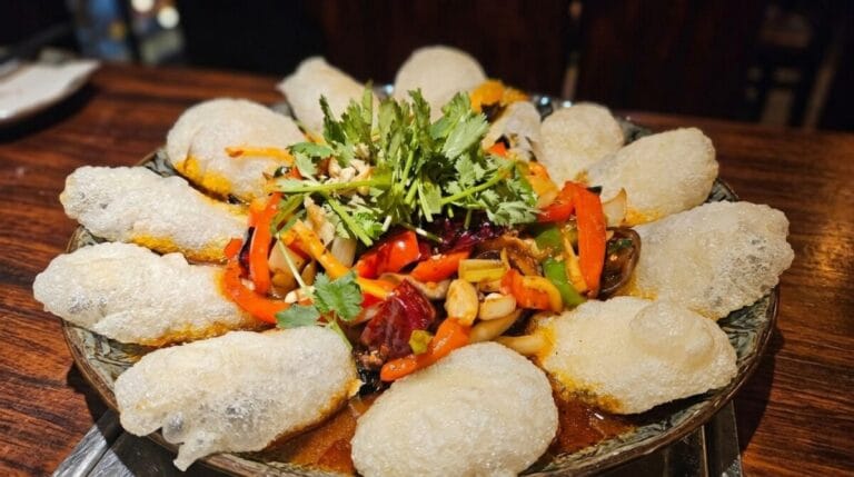 A close-up shot of the premium Uhwang Gaji (Fish-Flavored Eggplant) at Junghwa Bokchun, featuring crisp, airy fried eggplant pillows arranged around a vibrant stir-fry with bell peppers, chilies, and fresh cilantro.