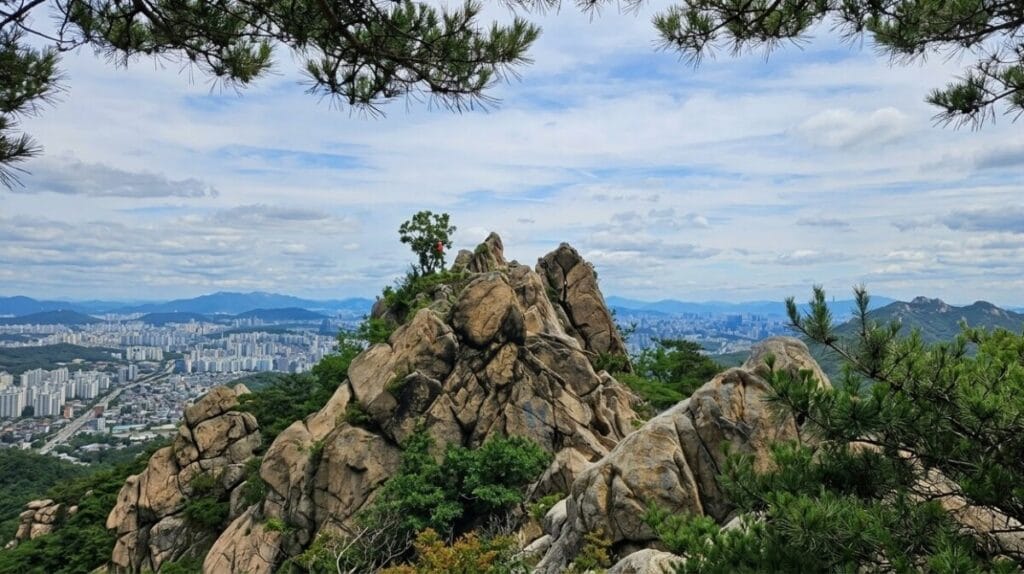 Hiker standing atop Gwanaksan's rocky summit with Seoul spread out below